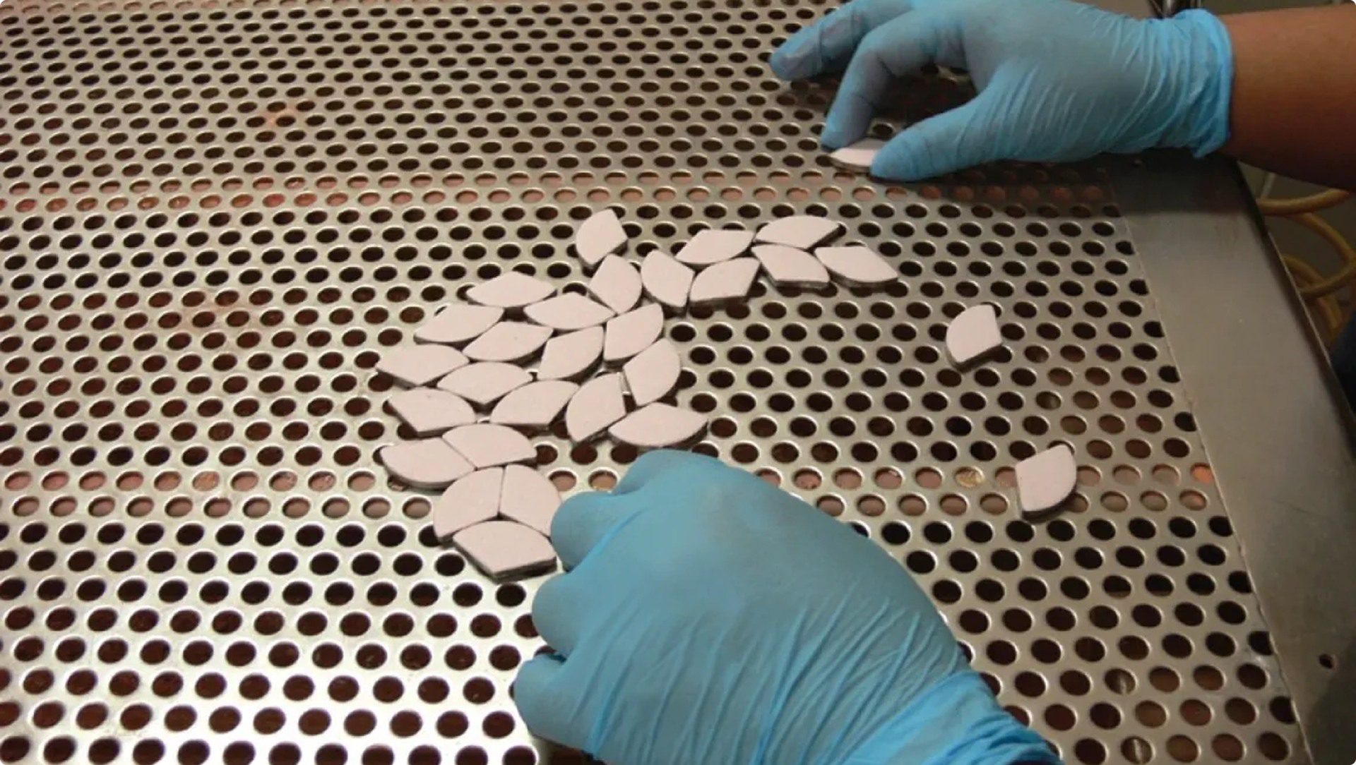 Gloved hands arranging small ceramic pieces.